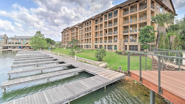 Een hotel met meerdere balkons, een steiger die in het water uitkomt, en een verzorgd gazon.