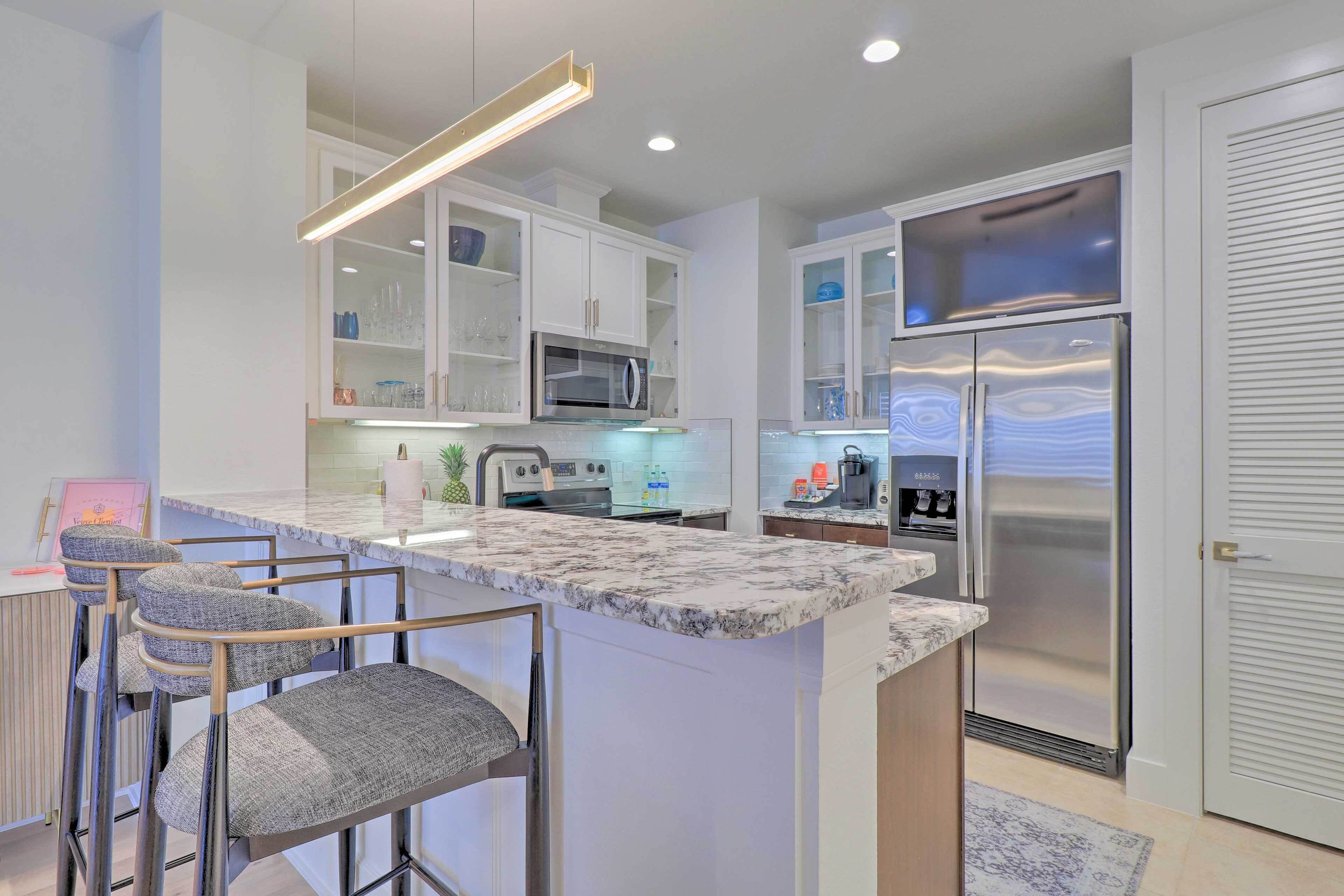 A modern kitchen with white cabinetry, a stainless steel refrigerator, and a marble countertop.
