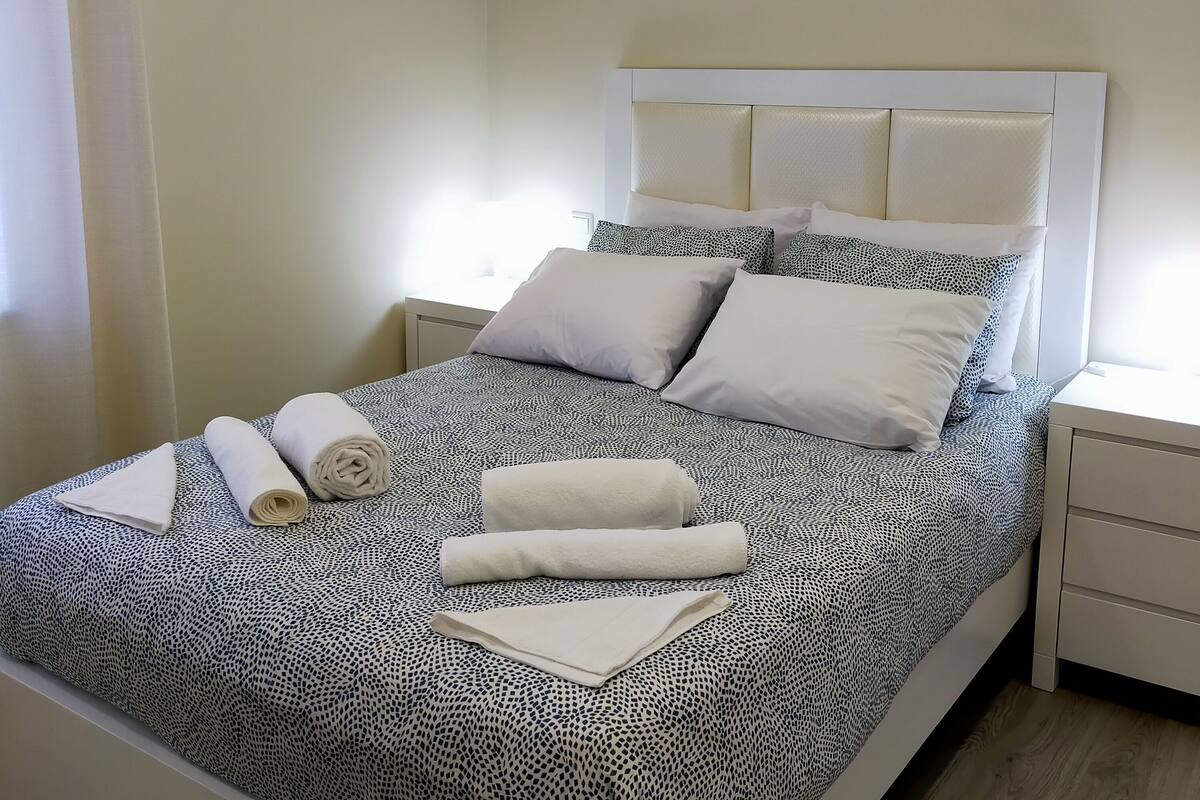 Una cama bien hecha con una colcha estampada, almohadas y toallas enrolladas.