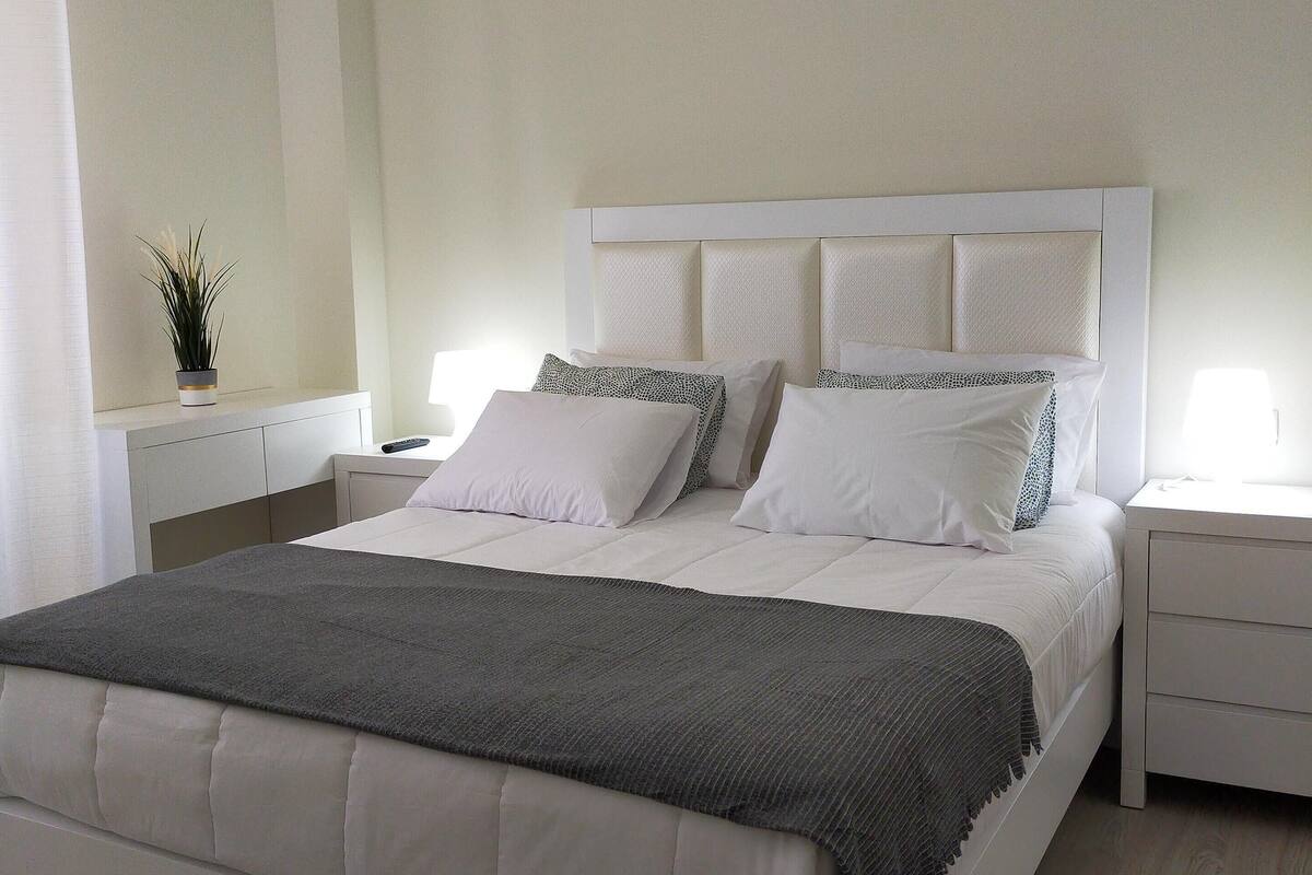 Un dormitorio ordenado con una cama grande, mesitas de noche, una lámpara colgante y una planta en maceta.