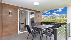 Une terrasse extérieure moderne, dotée d’une table et de chaises, d’une porte-fenêtre coulissante donnant sur l’intérieur et offrant une vue sur la verdure et les arbres.