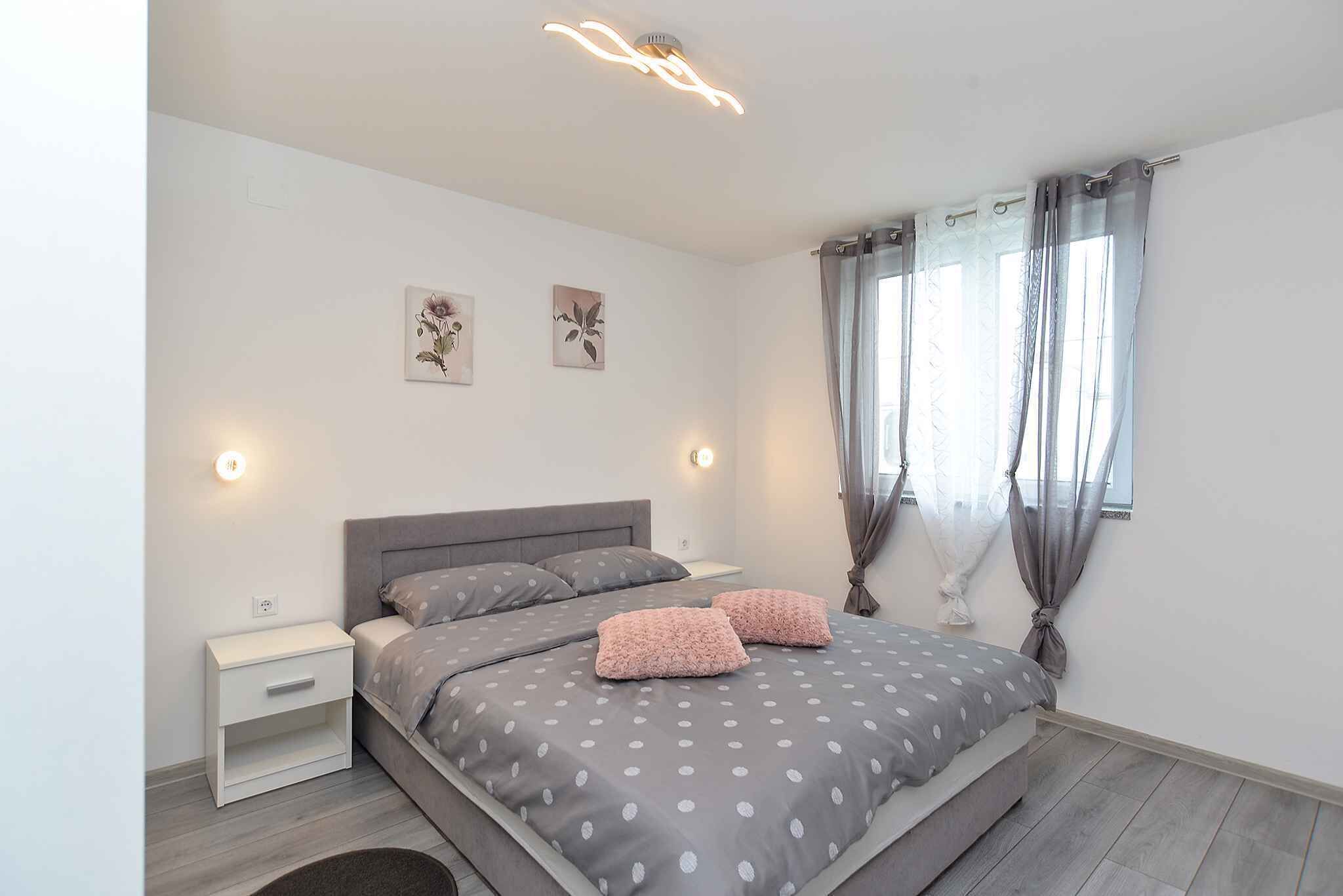 Quarto com cama, mesa de cabeceira, obra de arte na parede e janela com cortinas.