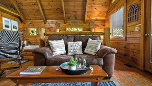 Ein gemütliches Blockhaus-Interieur mit einer braunen Ledersofa, einem Holztisch mit Buch und Tablett sowie einer Holzbalkendecke.