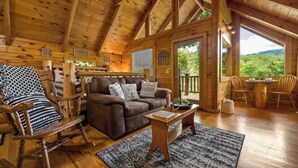 Ein gemütliches Cabin-Interieur mit Holzbalkendecke, einer braunen Ledersofa, einem Schaukelstuhl und einem Essbereich mit Tisch und Stühlen.