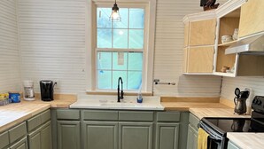 A kitchen with a window, wooden cabinets, a sink, a stove, and a hanging light fixture.