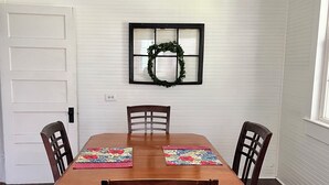 A dining room with a wooden table and four chairs, a white door, and a window with a wreath decoration.