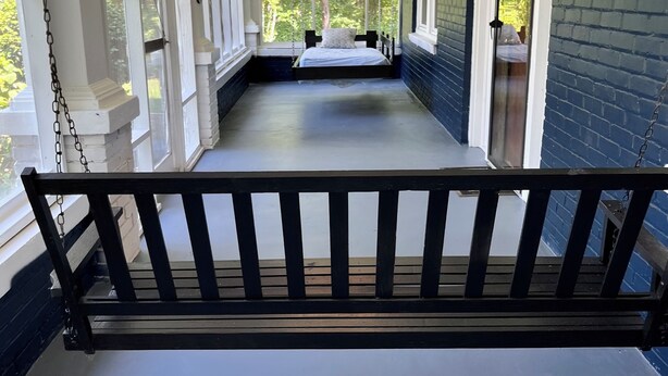 A porch with a swing, a bed with a pillow, and a chandelier.