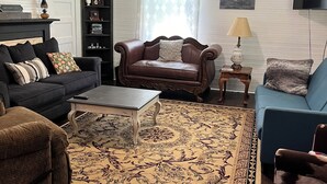 A living room with a dark brown leather sofa, a blue armchair, a patterned rug, and a wooden coffee table.
