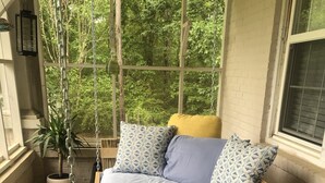 A wooden bed with a chain-link swing seat, positioned near a window with a view of greenery.