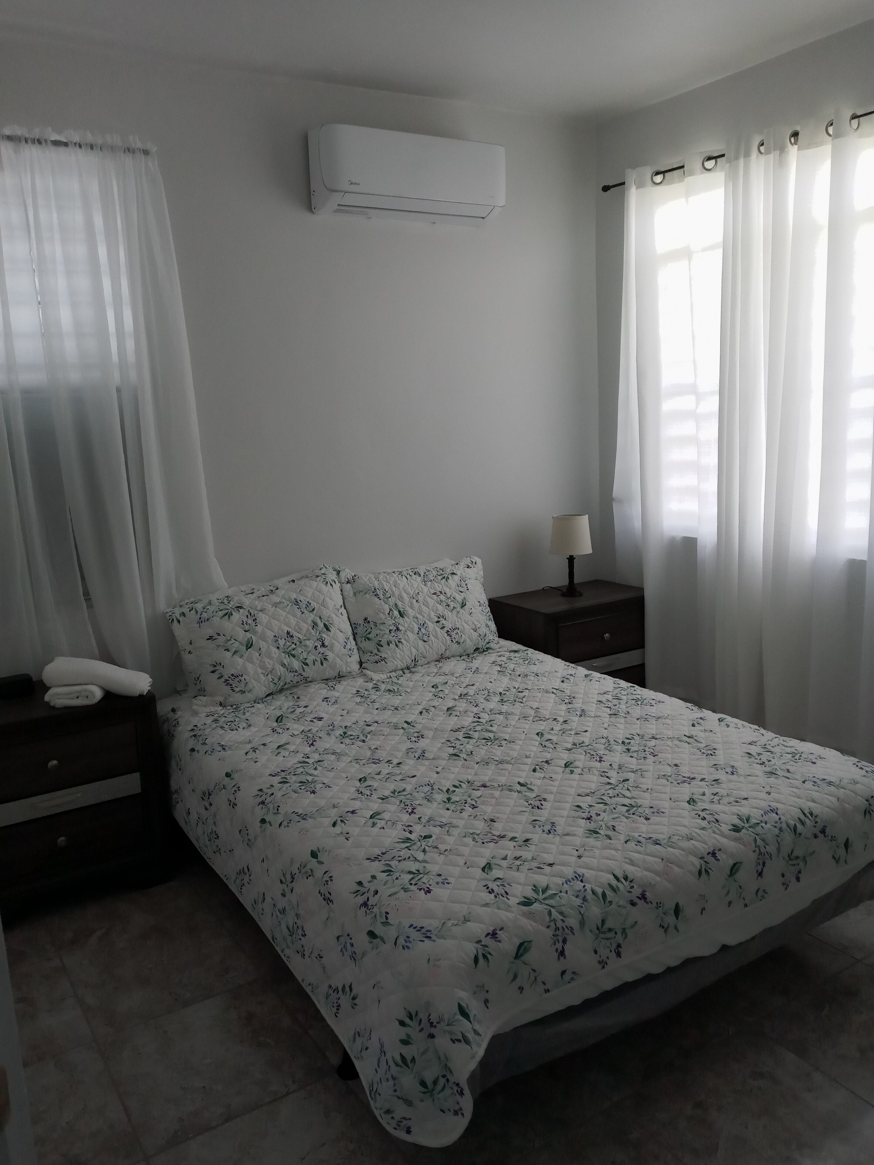 Ein Schlafzimmer mit einem Bett, einem Nachttisch, einer Lampe und einer Klimaanlage.