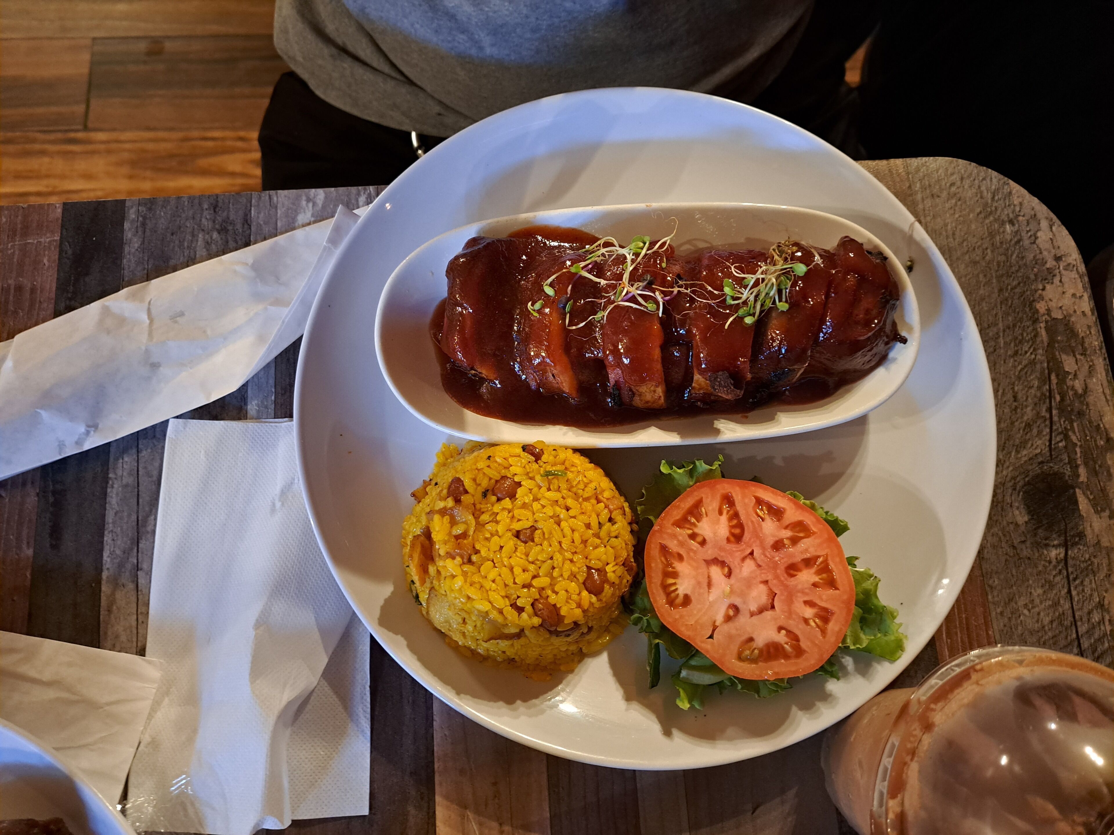 A plate with a grilled meat, yellow rice, and a slice of tomato on a wooden table.