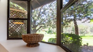 Una cesta tejida en un alféizar con vistas a un jardín y árboles.