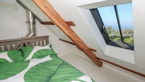 A bedroom with a sloped ceiling, a wooden beam, a window with a view, and a bed with leaf-patterned bedding. - Ty Mellen (Newport)