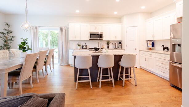 Een moderne keuken met witte kasten, een centraal eiland met krukken en een eethoek met een houten tafel en stoelen.