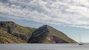 Paisagem costeira com uma colina imponente e um veleiro na água.