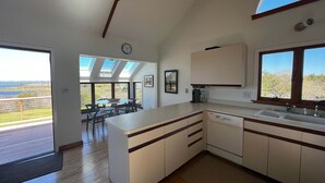 A modern kitchen with a large island, a dining area with a view, and a clock on the wall. - Chappaquiddick Getaway with stunning Ocean Views, walk to the beach (Edgartown)