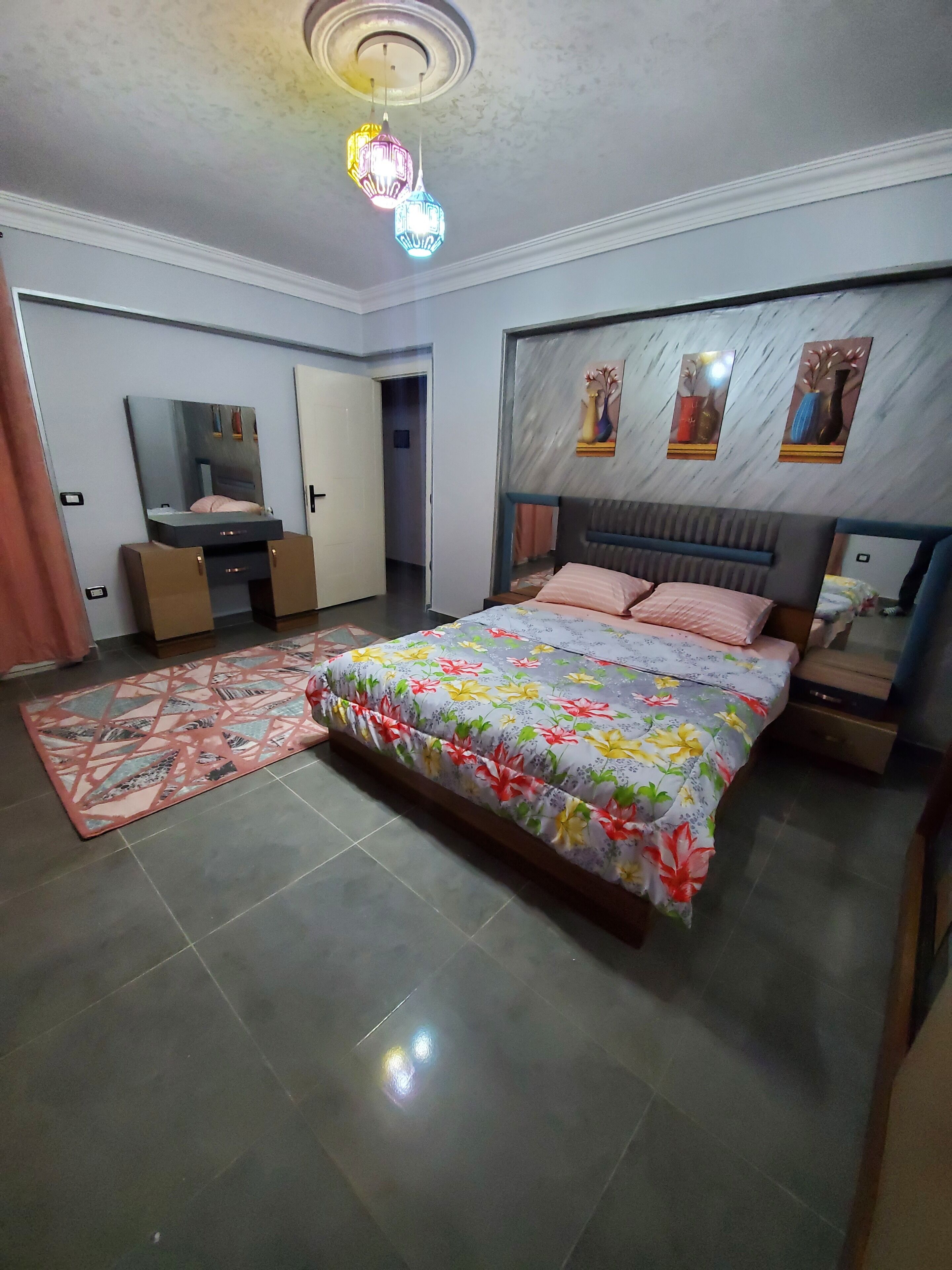 A bedroom with a bed, bedside tables, a dresser, a mirror, and a ceiling light fixture.