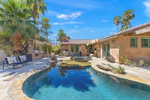 A pool area with a stone patio, lounge chairs, and a small building with a tiled roof. - Jaguar Villa - 6 BR in the Palm Desert hills! (Palm Desert)