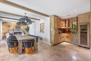A modern kitchen with wooden cabinets, a stone wall, and a dining area with a large table and chairs. - Jaguar Villa - 6 BR in the Palm Desert hills! (Palm Desert)