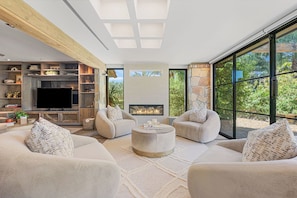 A modern living room with a fireplace, comfortable seating, and a large TV. - Jaguar Villa - 6 BR in the Palm Desert hills! (Palm Desert)