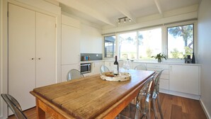 Una cocina moderna con armarios blancos, una mesa de comedor de madera y un amplio ventanal con vistas al exterior.