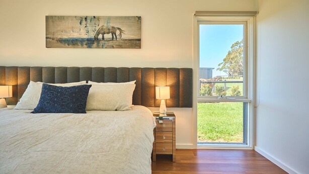 Un dormitorio con una cama grande, una mesita de noche con lámpara, una ventana con vistas al exterior y un cuadro en la pared.