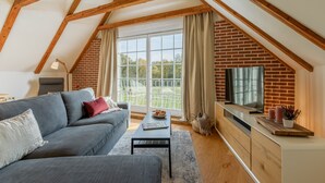 Una sala de estar moderna estilo loft con techo inclinado, un sofá gris, una mesa de centro y una pared de ladrillo con un ventanal grande.