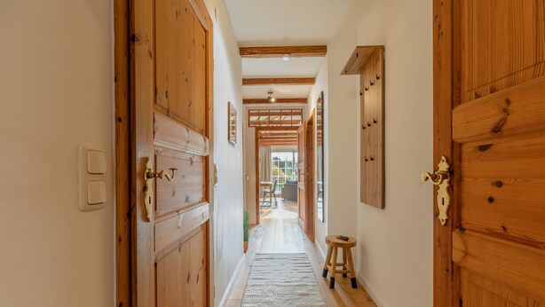 Un pasillo de madera con un tapete, un taburete y una puerta con pomo de latón.