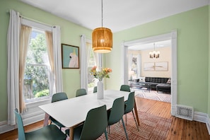 Un espace repas avec une table blanche, des chaises vertes et un luminaire suspendu.