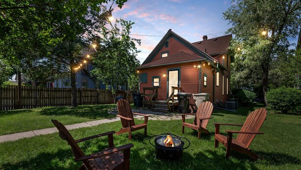 Ein Garten mit Feuerstelle, Holzstühlen und einem Haus mit Veranda.
