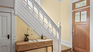 Eine Treppe mit weißen Balustern, ein Holzkonsolentisch mit einer Vase und Papieren sowie eine Holztür mit Glasfeldern.