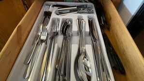 Un cajón de cocina con cubiertos ordenados, un recipiente azul para utensilios y una olla de cerámica blanca sobre la encimera.