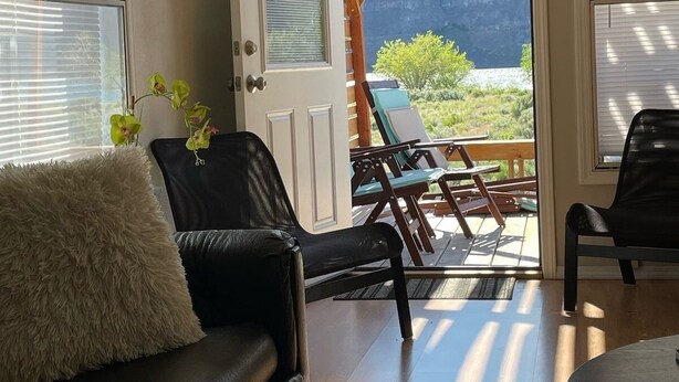 Una sala de estar con un sofá de cuero negro, un cojín mullido y vistas a un patio con mobiliario exterior.