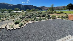 Un área ajardinada con un sendero de grava, una valla de madera y una vista al lago y las montañas al fondo.