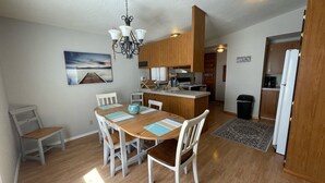 Un comedor con una mesa y sillas de madera, una cocina al fondo y un cuadro en la pared.