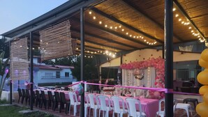 An outdoor event area with tables and chairs, a stage, and string lights.