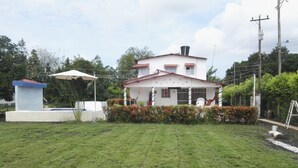 A house with a white exterior and red roof, surrounded by a well-maintained lawn and a small garden with red flowers.