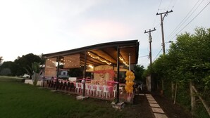 A covered outdoor area with tables and chairs, power lines, and greenery.
