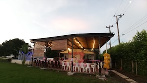 An outdoor event space with tables and chairs, a covered area with string lights, and a decorative arch.