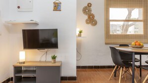 Una sala de estar moderna con un televisor de pantalla plana, una mesita con un frutero, una lámpara de pared y un elemento decorativo en la pared.