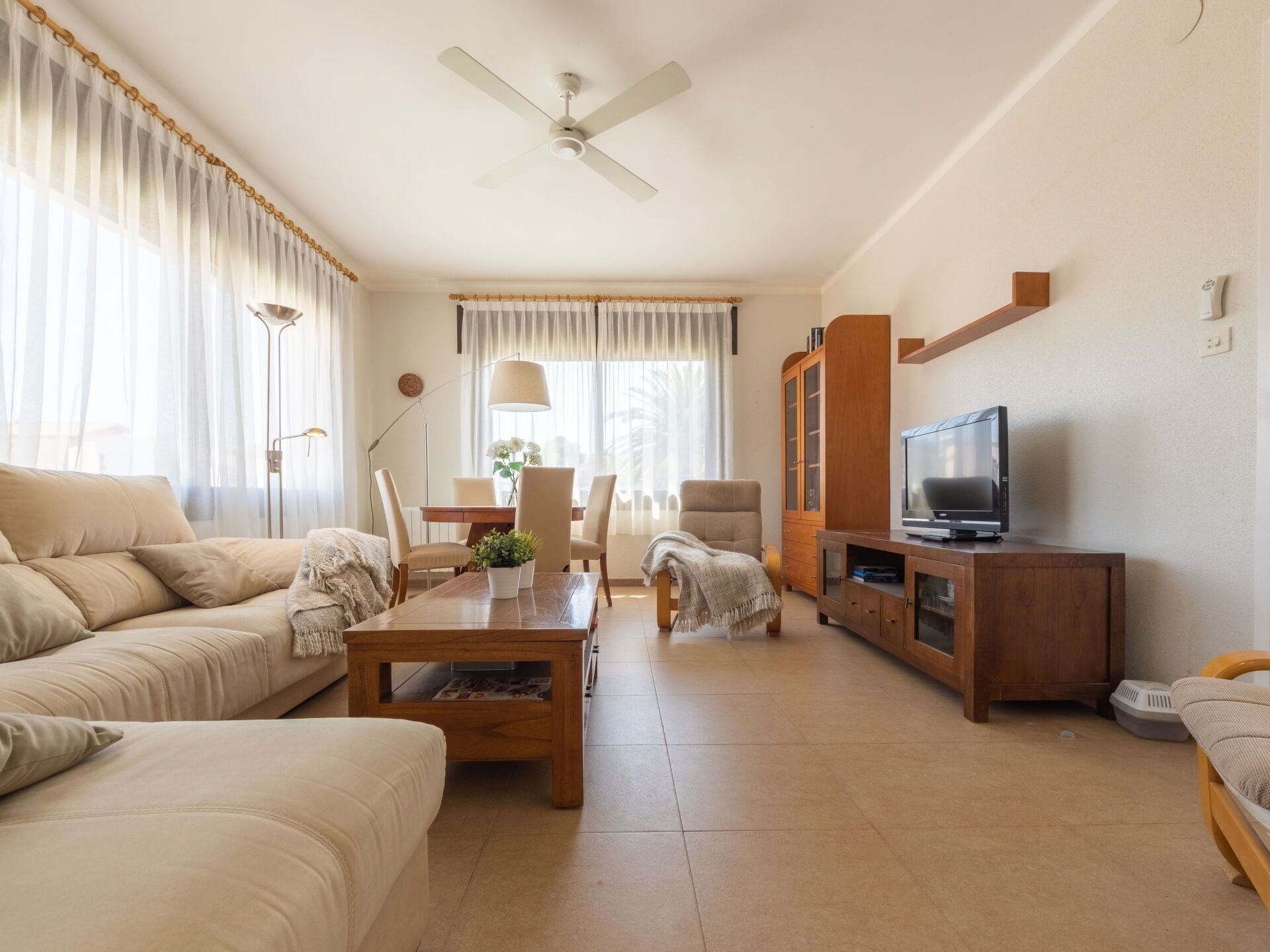 A living room with a sofa, coffee table, TV stand, and a dining area with chairs and a table.