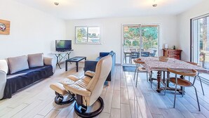 A spacious living area with a sofa, a massage chair, a TV, and a dining table with chairs. - Stunning private villa for 6 guests with WIFI, TV, terrace and pets allowed (Montalivet-les-bains)