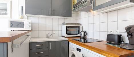 Una cocina compacta con gabinetes grises, microondas, tostadora, cafetera y lavadora.