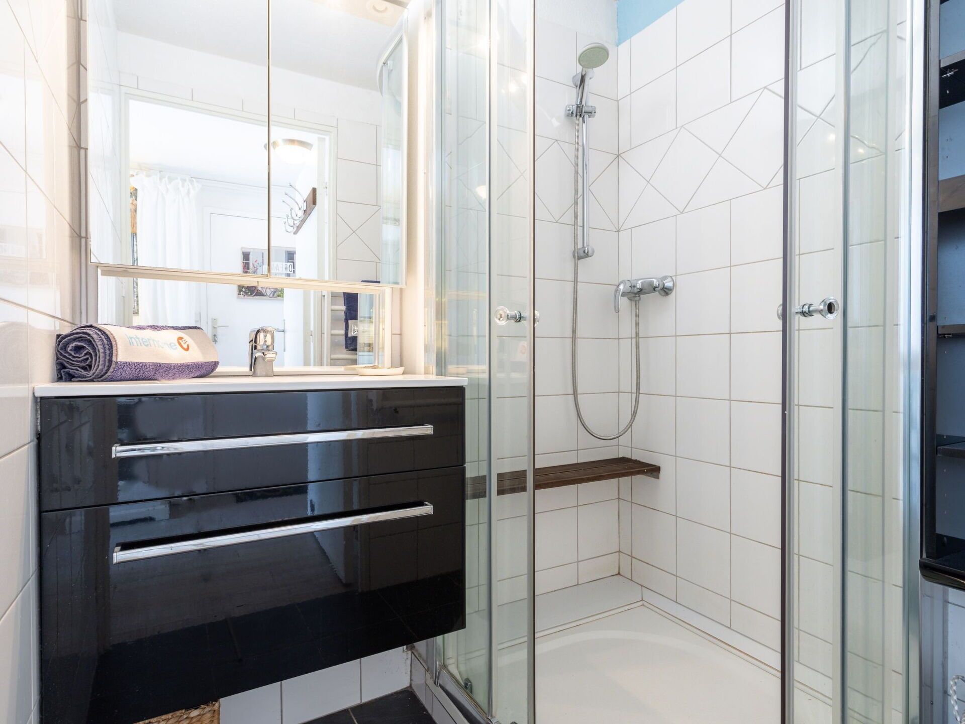 A modern bathroom with a glass shower enclosure, a black vanity with a mirror, and a white tiled wall.