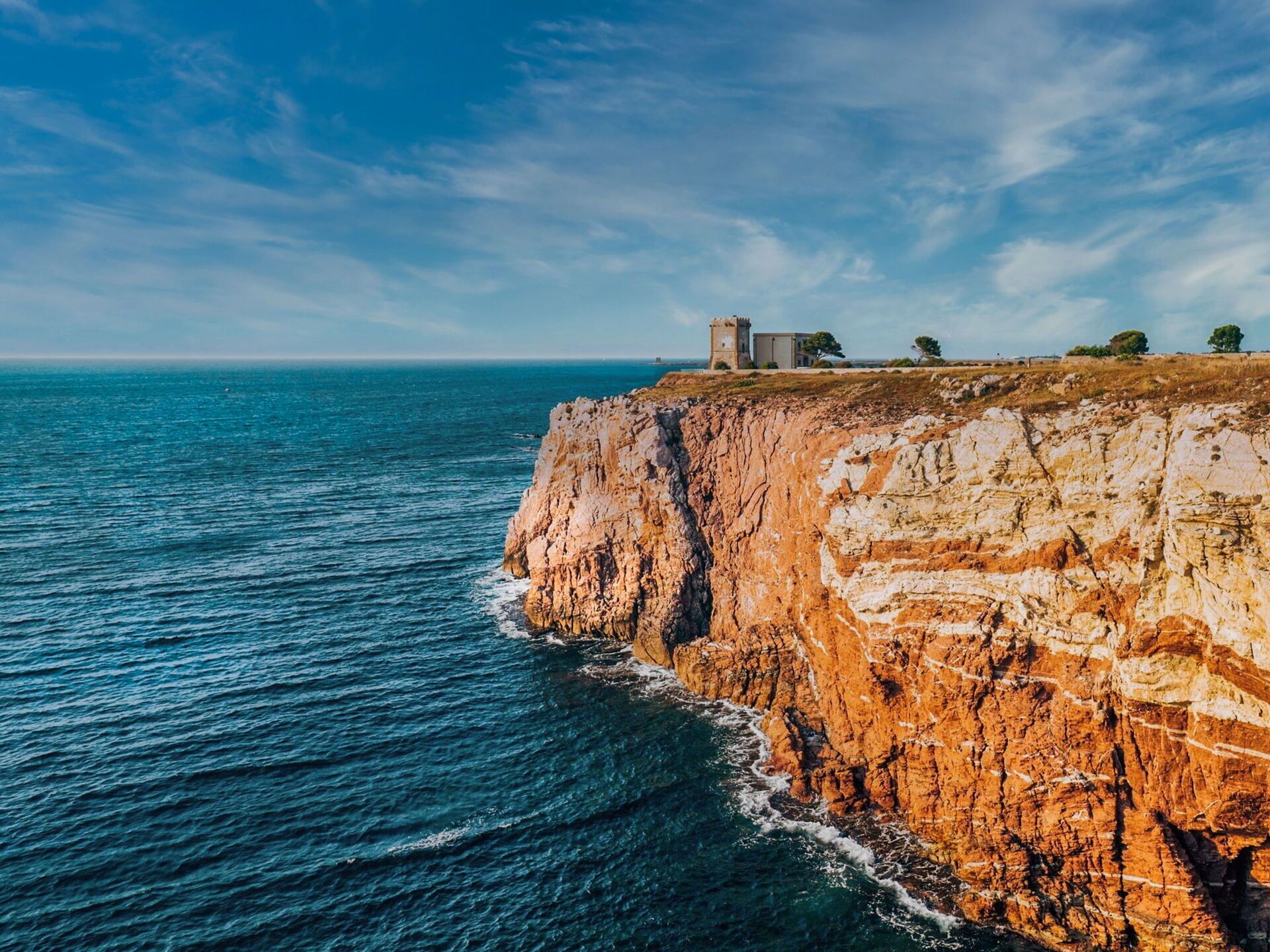 A coastal cliff with a tower and a building on top, overlooking the sea.