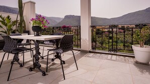 Een terras met een tafel en stoelen, plantenbakken en uitzicht op bergen.