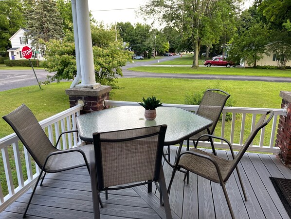 A covered outdoor patio with a glass table and four chairs, a potted plant, and a view of a residential street. - Minutes from Niagara Falls in a Historic Village (Lewiston)