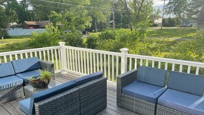 Une terrasse couverte, aménagée avec des meubles en osier et dotée d’une rambarde blanche.