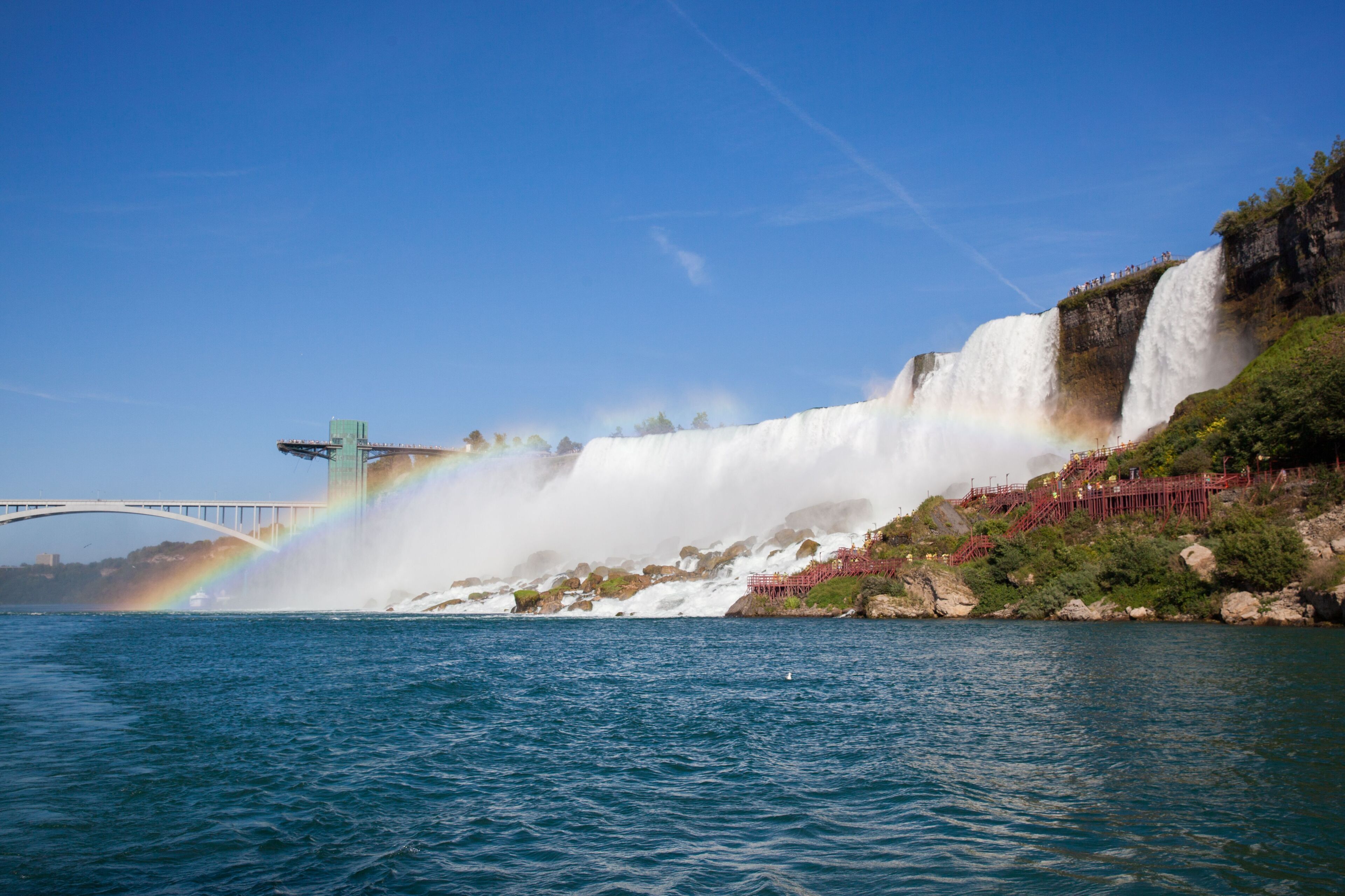 Een waterval met een regenboog, een brug en een rotsachtige oever.