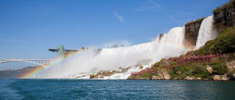 Een waterval met een regenboog, een brug en een rotsachtige oever.